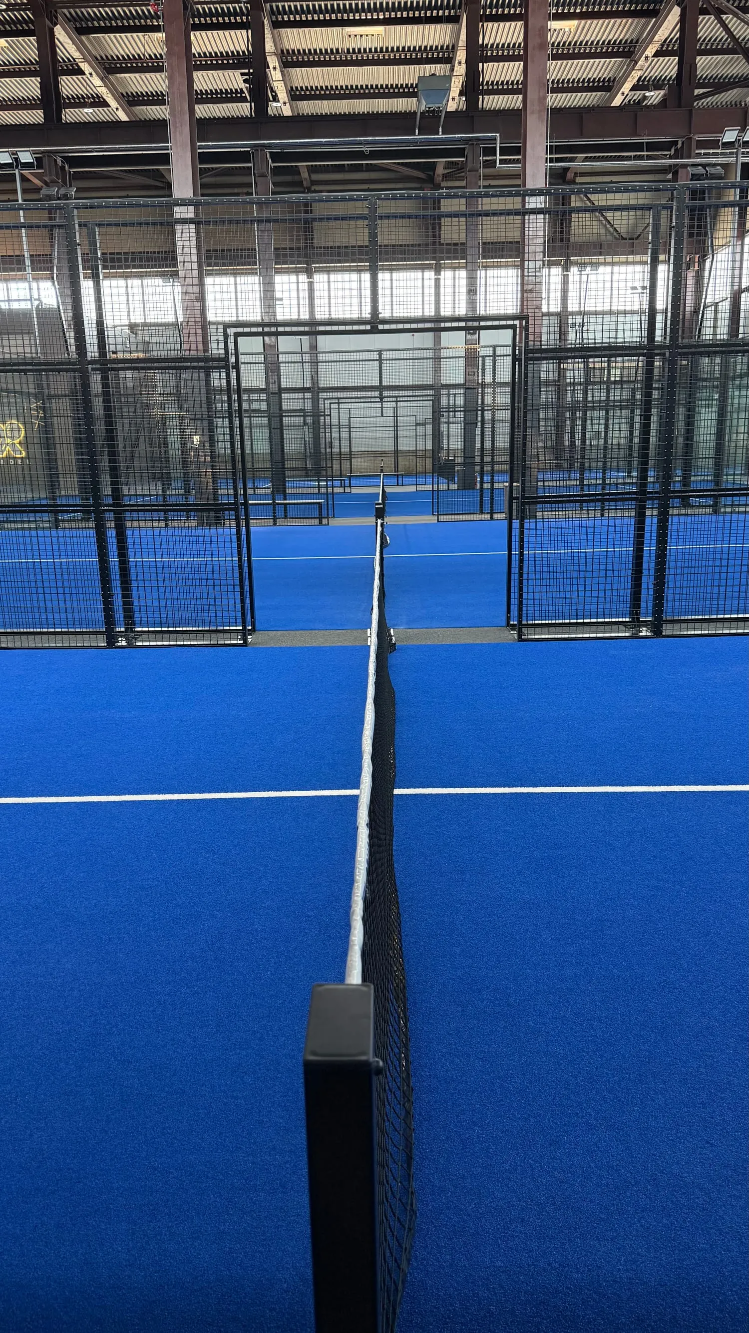 Padel laukums no spēlētāja skatpunkta — tīkls un zilais segums
